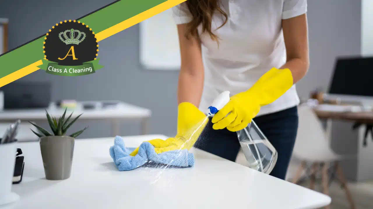Woman cleaning a desk with gloves on and Class A Clean logo banner in top left.